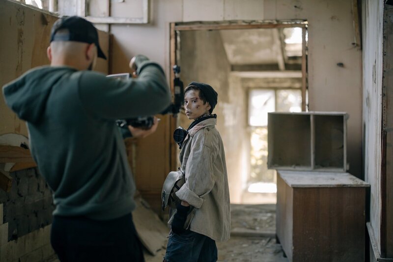 a guy with hood filming young dirty boy surrounded by apocaliptical