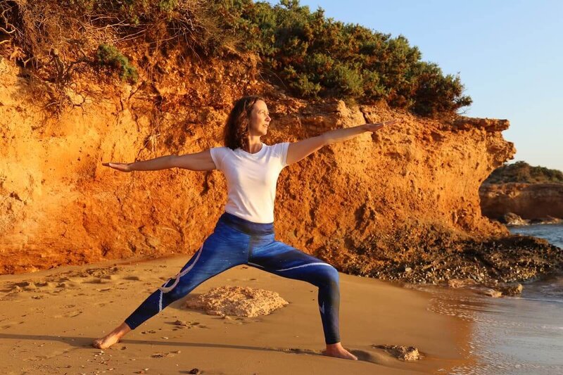 Student demonstrating Warrior 2 pose with ocean waves in background.