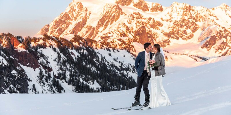 Wedding couple kissing in front of the mountain on skis in snowy backdrop