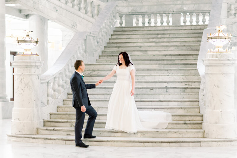 Elegant couple walking down a grand staircase in the Utah State Capitol Building  during their first look by Andria Joleen Photography a Utah Wedding Photographer