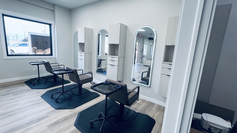 Modern salon styling stations at Tailored + Co featuring sleek neutral-toned cabinetry, arched mirrors, and plush styling chairs in a clean, luxurious setting. Designed to reflect high-end sophistication and comfort.
