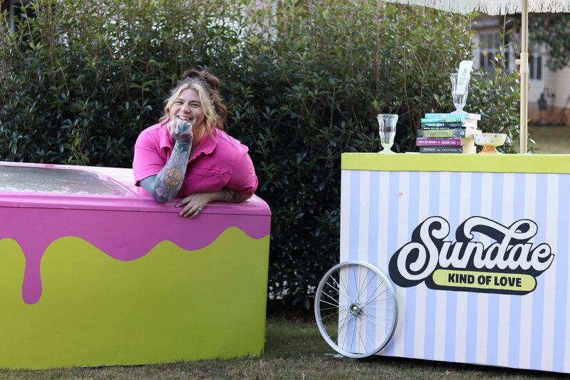 A woman leaning out of an ice-cream freezer laughing.