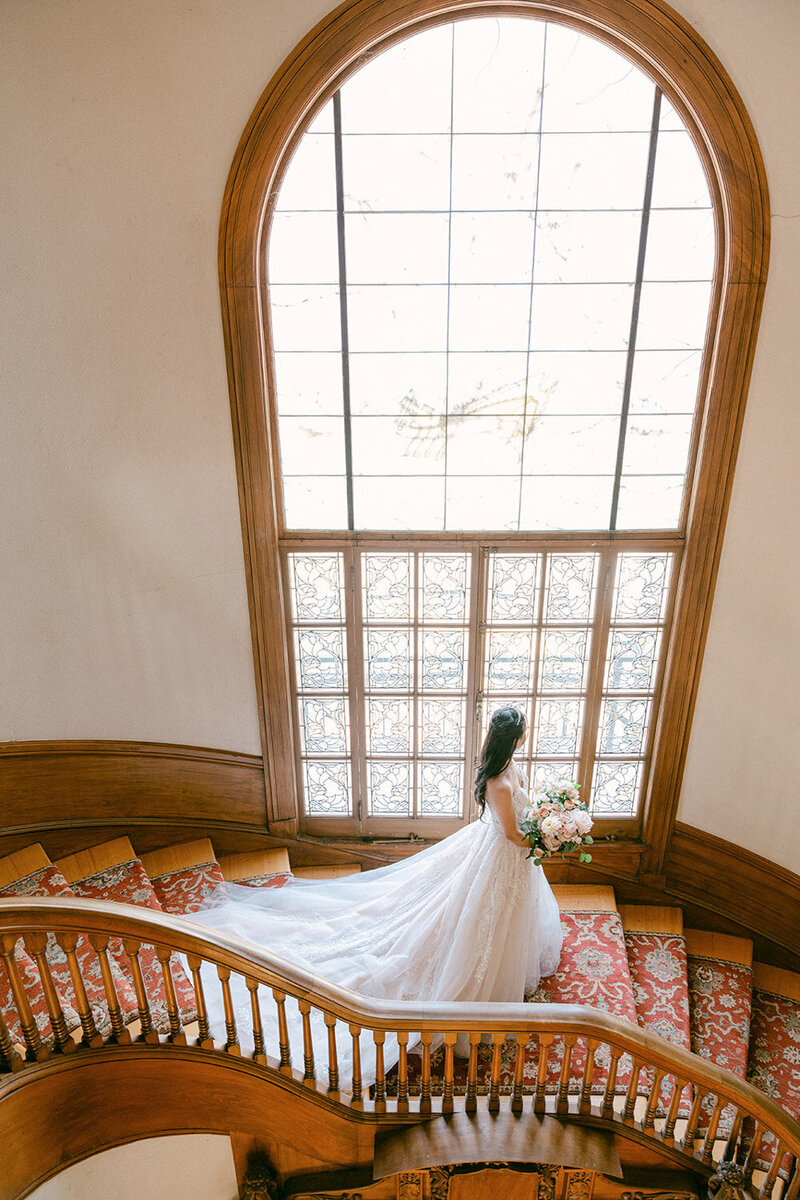 Bride standing on staircase with flowing wedding gown