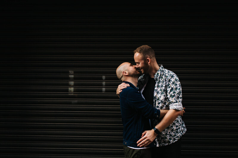 A same sex couple kissing  in front of an urban backdrop in Manchester 5: Title: Fun City Wedding