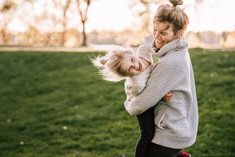 A mom hugs her daughter tummy to tummy while spinning in circles and laughing at Lake Harriet in Minneapolis, Minnesota.