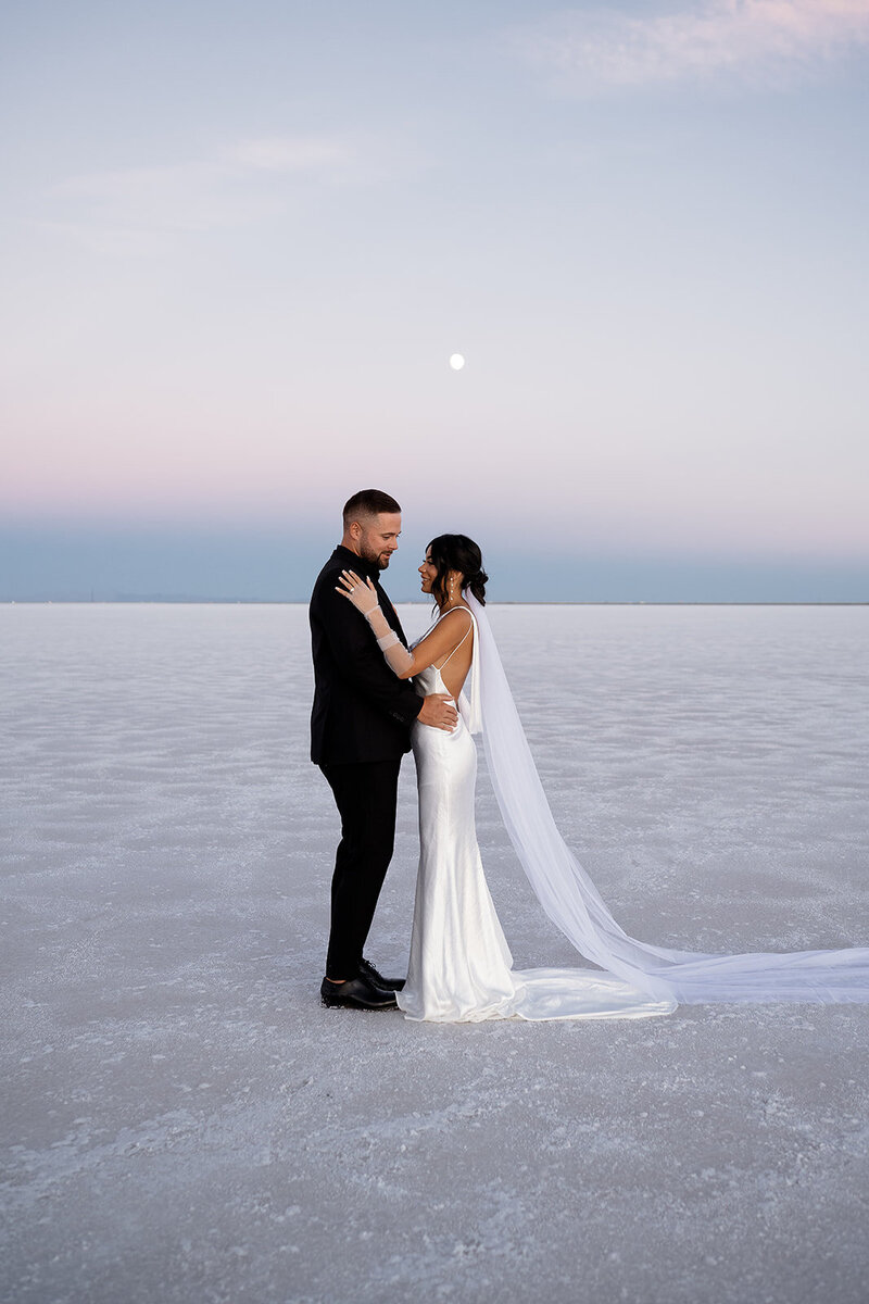 Couple in wedding attire during a beautiful twilight elopement on the salt flats with the moon in the background.
