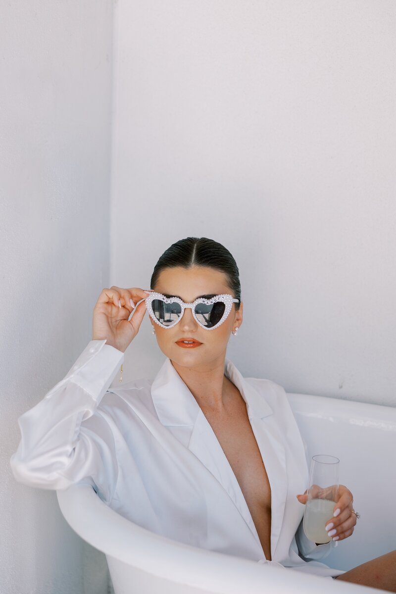 Bride wearing sunglasses and drinking champagne before wedding day