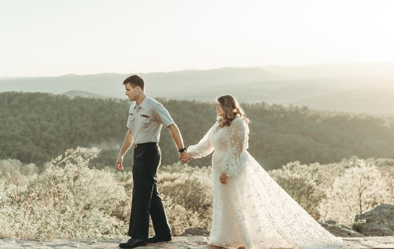 Beautiful mountain wedding outside of Charlotte on Asheville Blueridge Parkway. Young man in Army outfit and bride in beautiful dress holding hands at sunset