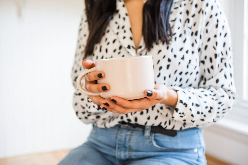 a closeup of a woman with black nail polish holding a large white coffee cup