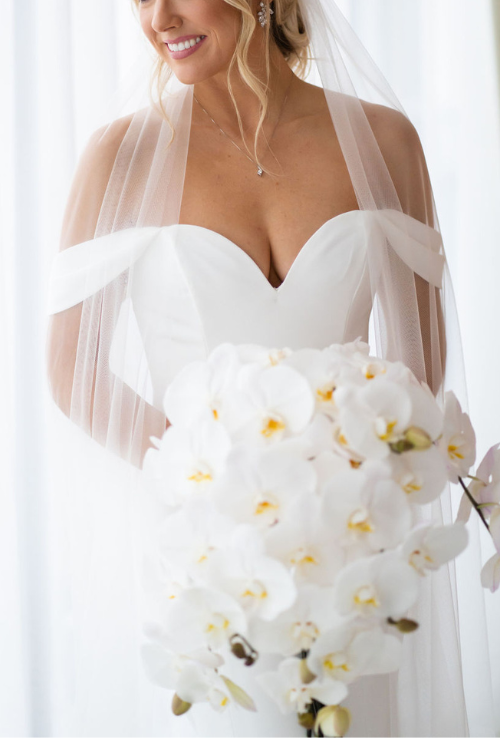 Bride with off the shoulder wedding dress holding white orchid bouquet