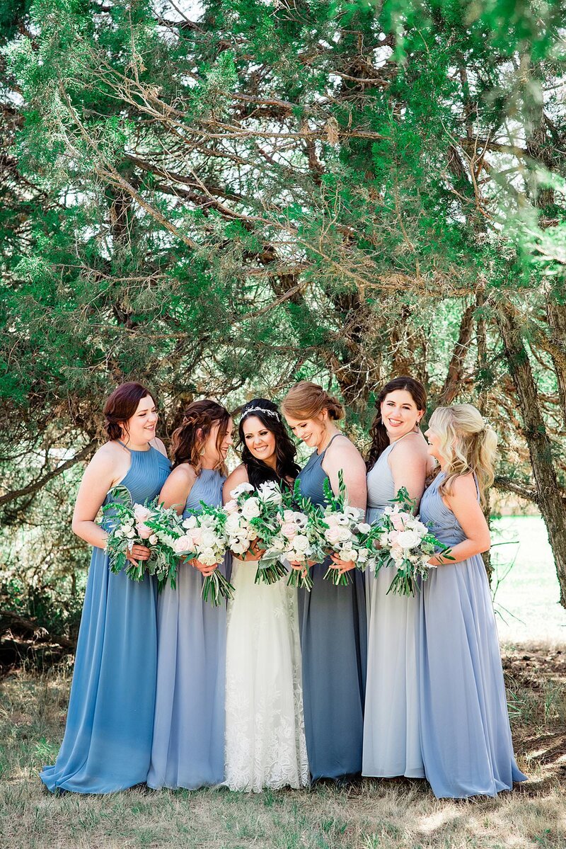 Bridesmaids wearing shades of dusty blue surrounding bride and smiling together