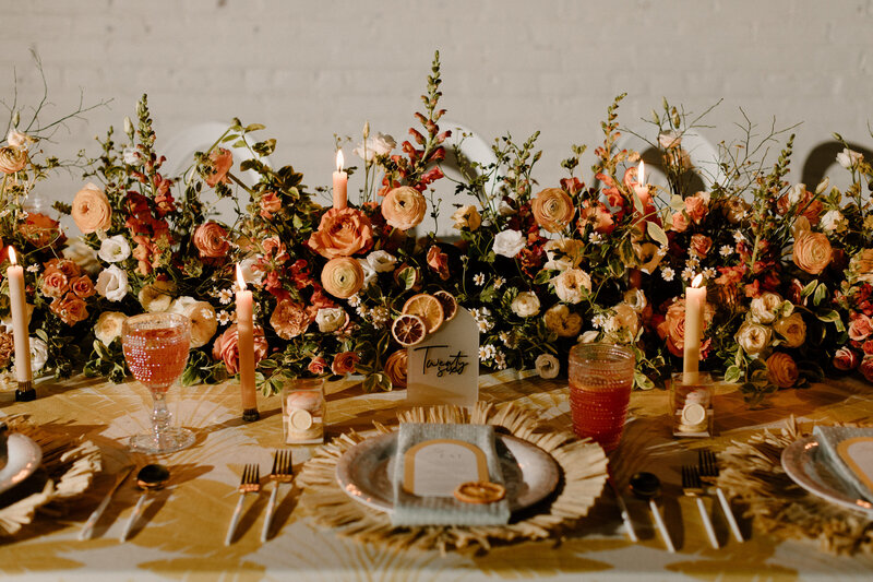 A wedding reception table with pink drinks and colorful floral arrangements 
