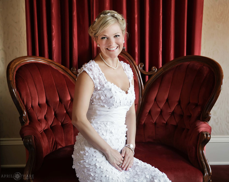 Bride poses for a simple portrait on a red velvet settee at Hotel Boulderado