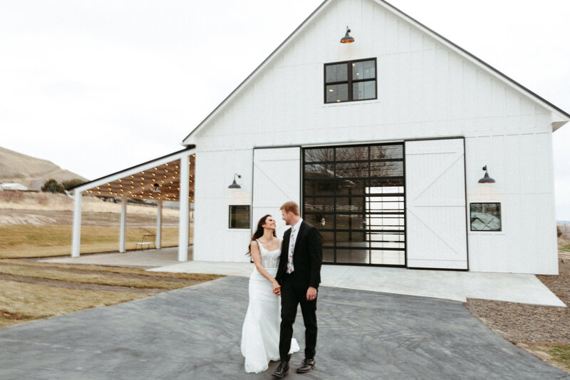Couple walking away out front of the White Barn, looking at each other.