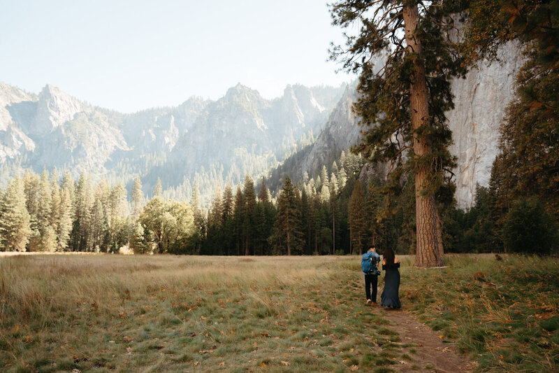 Couple walk along a path in a green meadow surrounded by granite formations, the perfect place for a yosemite wedding