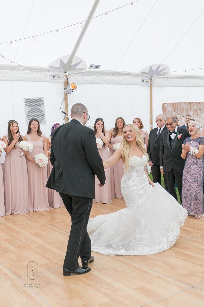 Bride and groom dancing with bridal party in background. Brides face has a big smile.