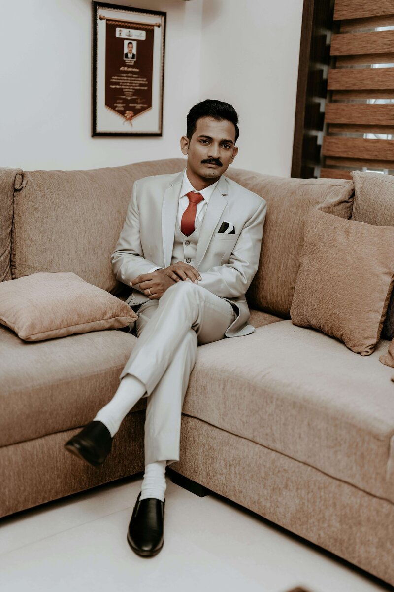 A man wearing a suit sits on a sofa representing the luxe and diverse nature of the bridal show by The Crush Collective.