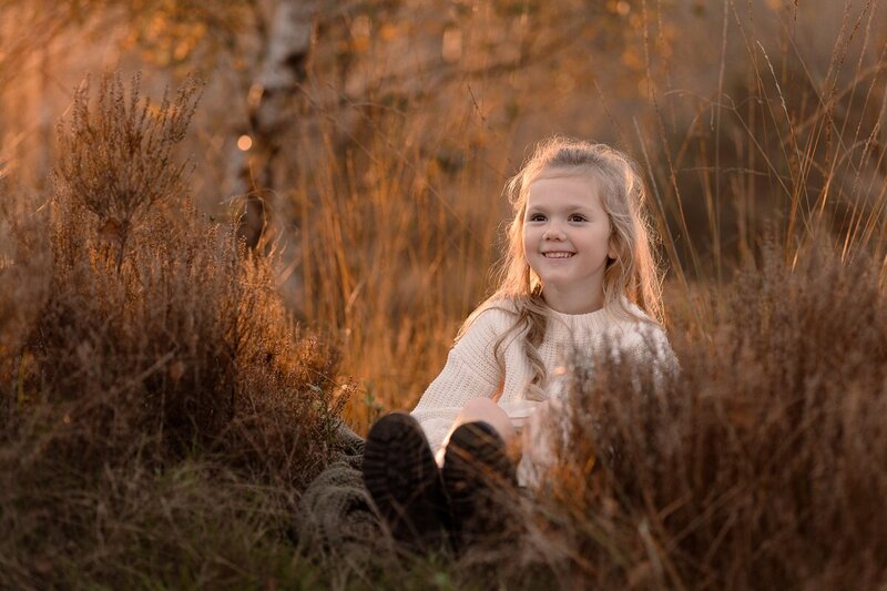 Meisje in het hoge gras zittend tijdens de zonsondergang met een grote glimlach op haar gezicht