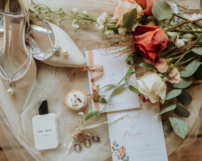 Wedding stationery surrounded by wedding bouquet, rings, the bride's shoe and trinkets.