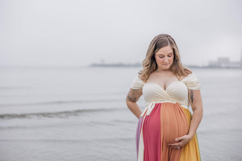 Pregnant woman in rainbow dress looks down at her belly.