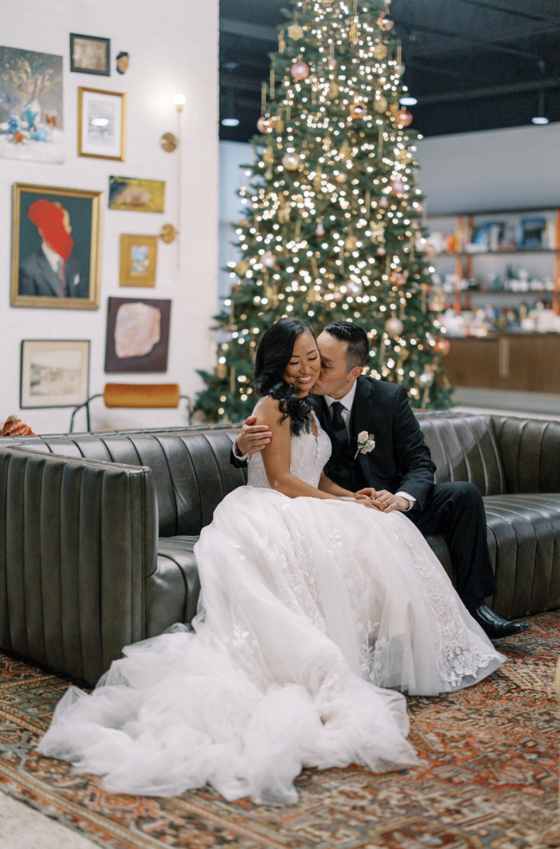 Catholic bride and groom embrace in front of Christmas tree at their wedding reception in Pensacola, Florida.