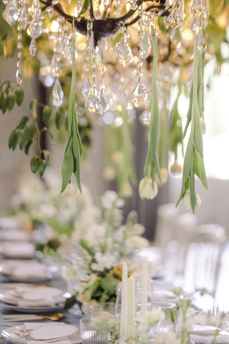 A dreamy romantic tabletop setting for an elegant wedding containing flowers, greenery, tulips, candles, glassware and crystals.