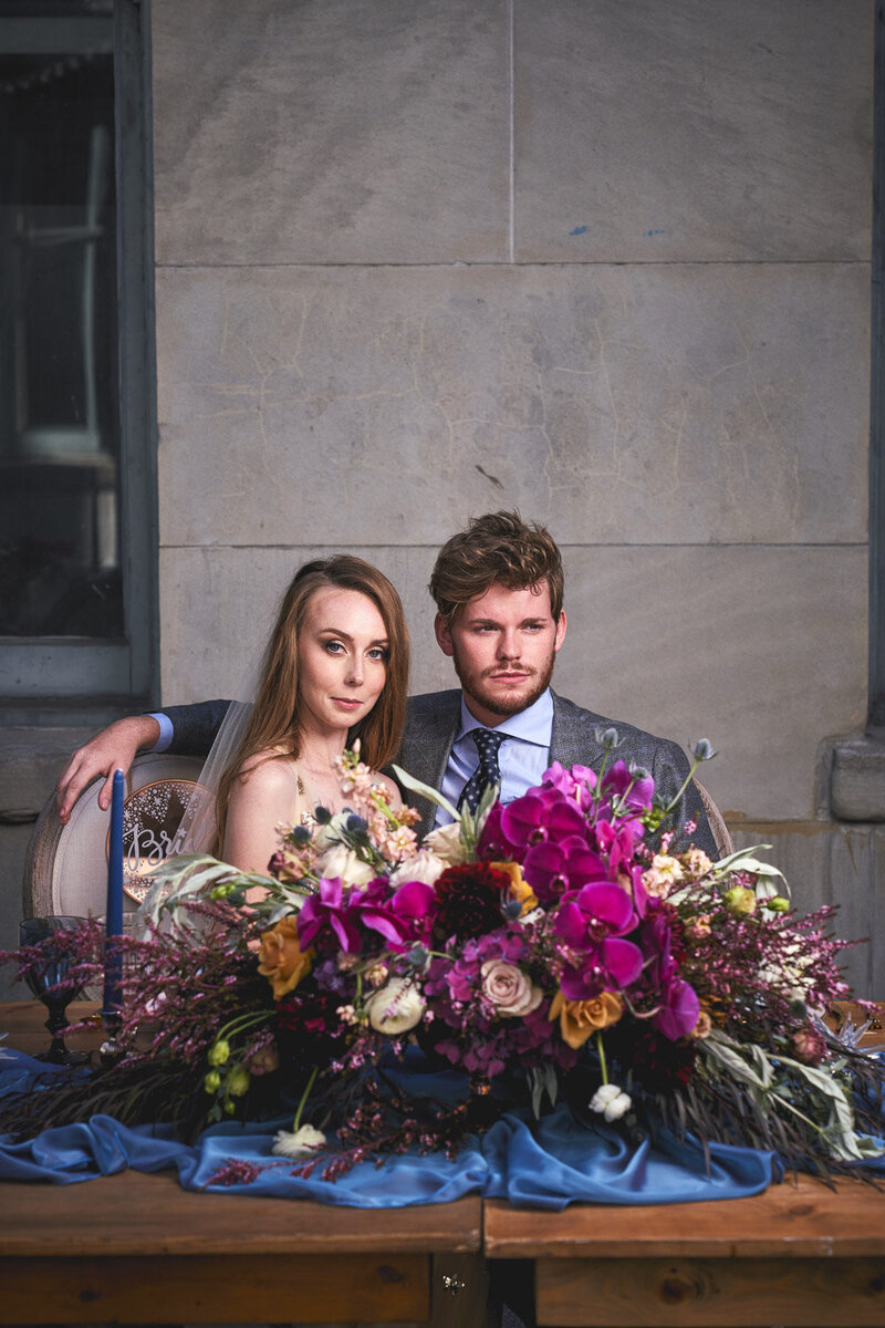 Couple seated at sweetheart table with vibrant floral centerpiece