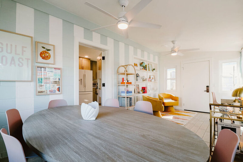 sunroom with teal and white striped walls, dining table with pink chairs