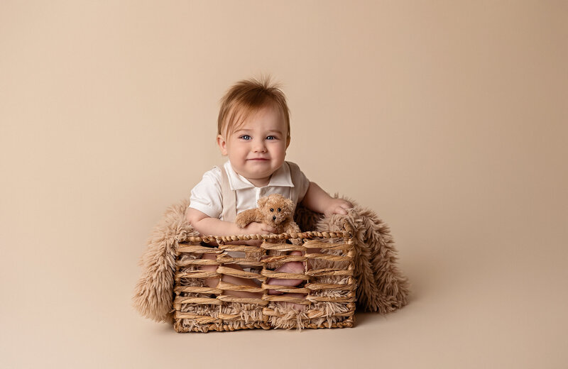 little boy on tan backdrop holding a teddy bear