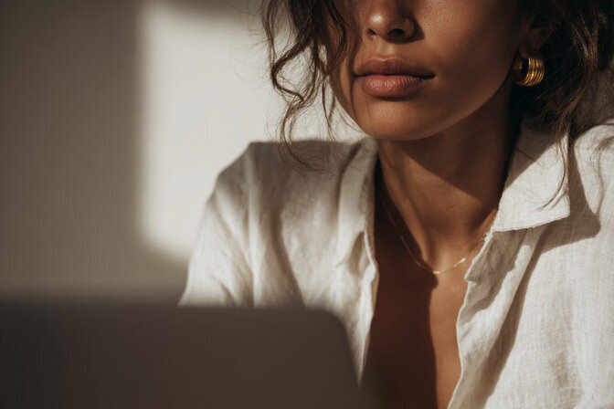 Editorial portrait of a female designer working on a laptop in soft natural light, representing Kathalyst Design Studio’s refined and intentional approach to strategic branding and custom Showit website design.