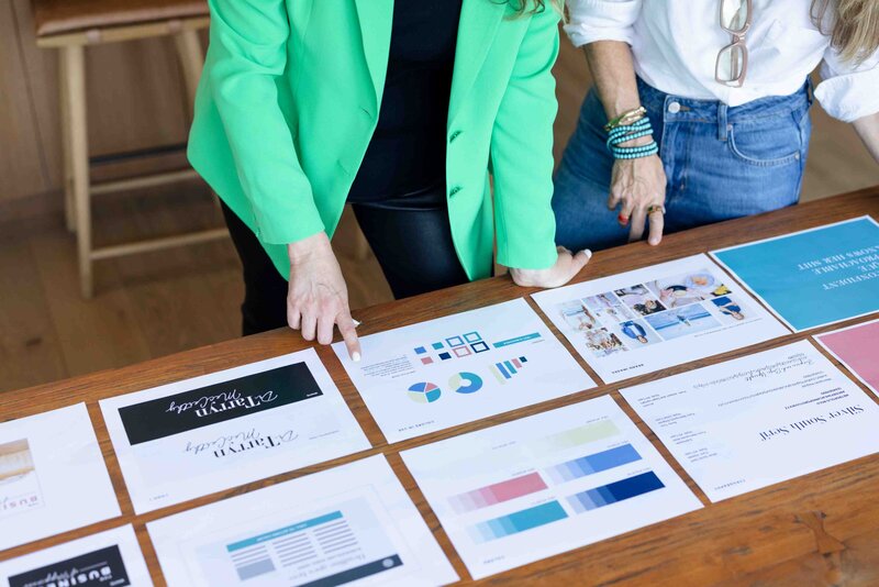 Brand strategist in emerald green blazer reviewing client brand strategy documents featuring color palettes, data charts, and visual identity elements