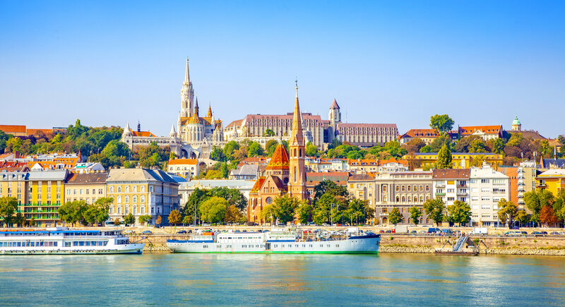 An enchanting European town with a river and riverboats in front of it.