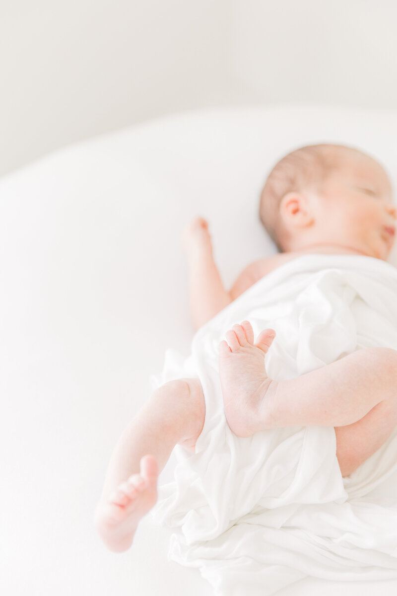 A newborn baby lays on a white bed wiggling