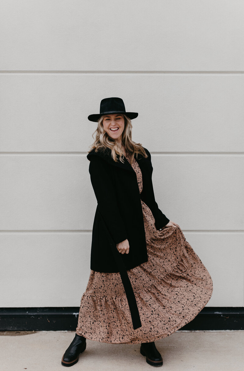 woman wearing long dress and black coat with black hat while smiling
