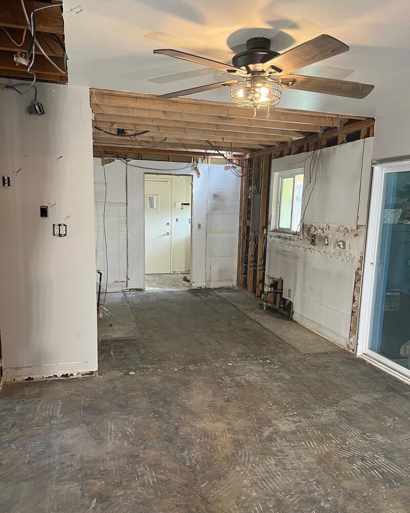 A room in the middle of remodeling with exposed ceiling rafters and no flooring.