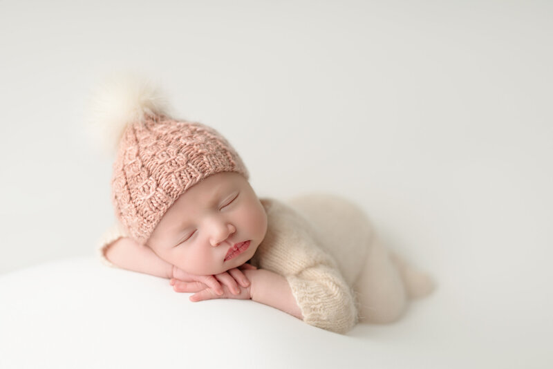 Newborn girl wearing pink knit hat and posed on white backdrop – timeless and cozy newborn image from Paris, Ontario.
