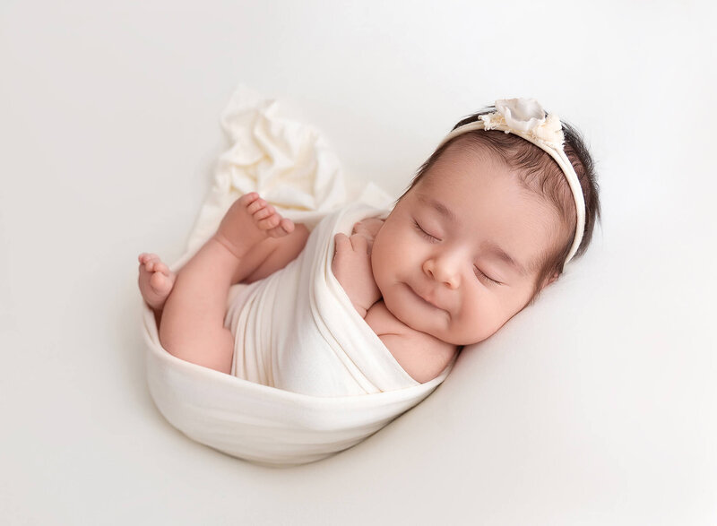 Newborn baby wrapped in white smiling at het photo session with Rochel Konik Photography