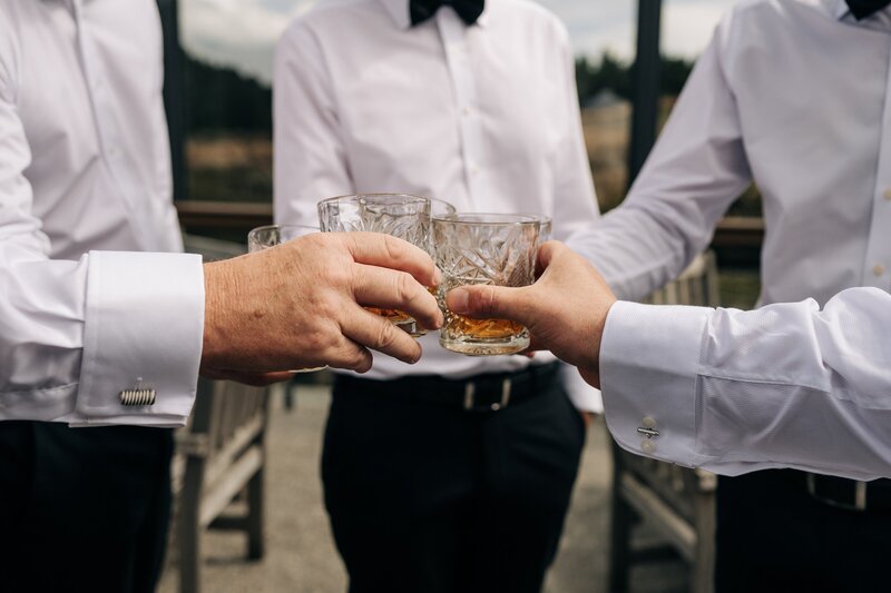 four men in white shirts and black bowties cheers whiskey glasses at terrace downs