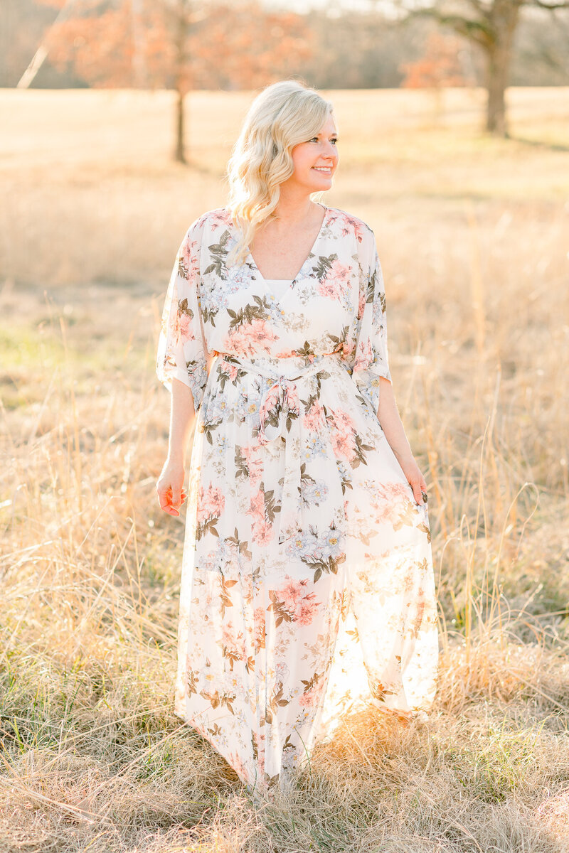 Ashley Gregory a Brandon, MS Newborn Photographer walking in a field with a beautiful white dress with florals in the sunlight.