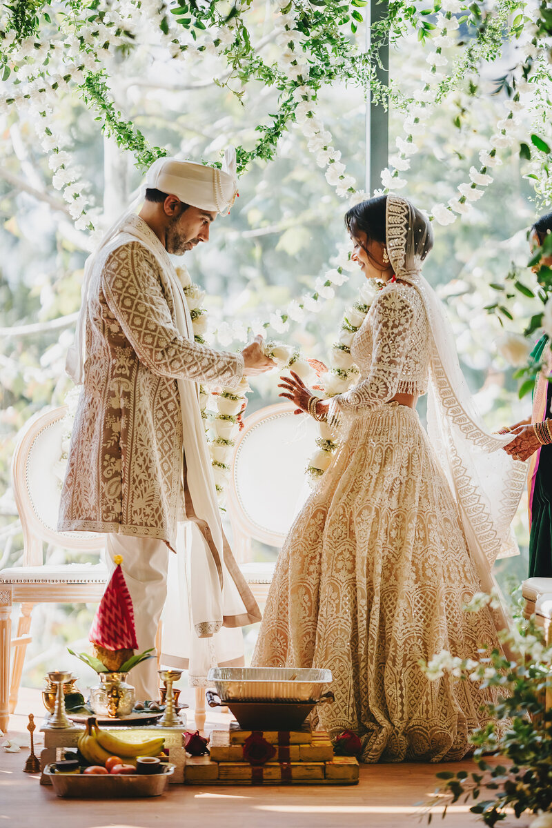 Indian bride and groom giving each other flower garland necklaces during Hindu wedding ceremony