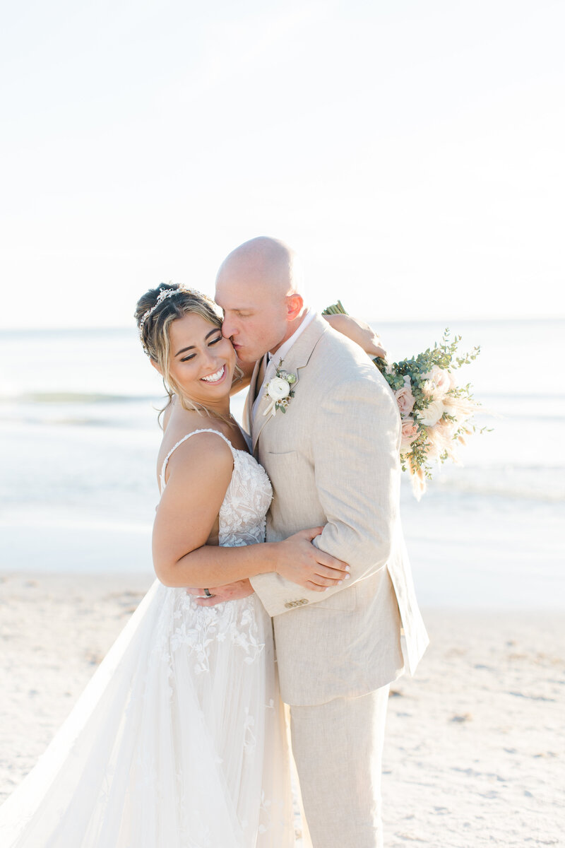 groom kissing bride on the cheek at the beach