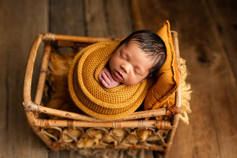 Newborn baby boy wrapped in an apricot colored wrap.
