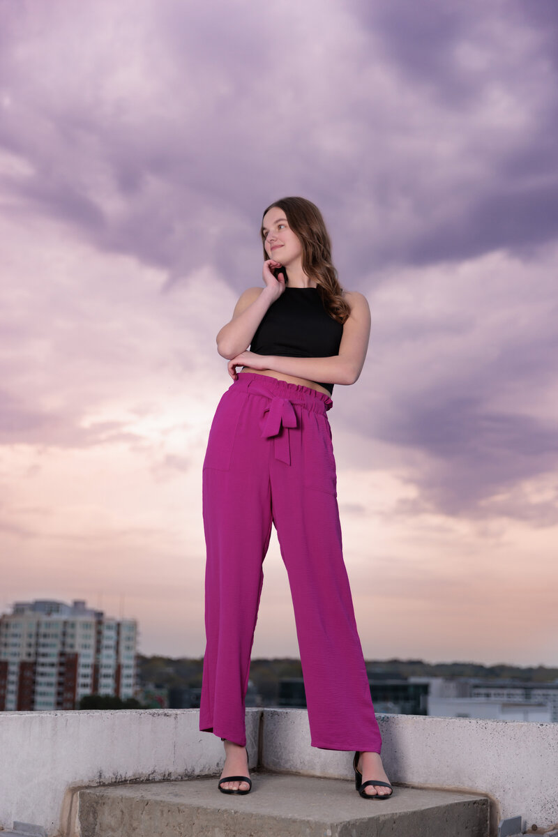 Powerful high school senior portrait at sunset on a Raleigh rooftop wearing pink pants.