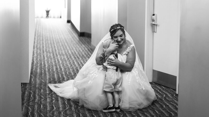 Bride stoops down to hug her son in hotel hallway