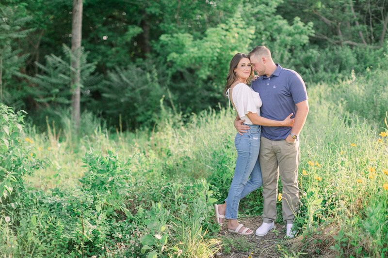 An engaged couple poses in a green field