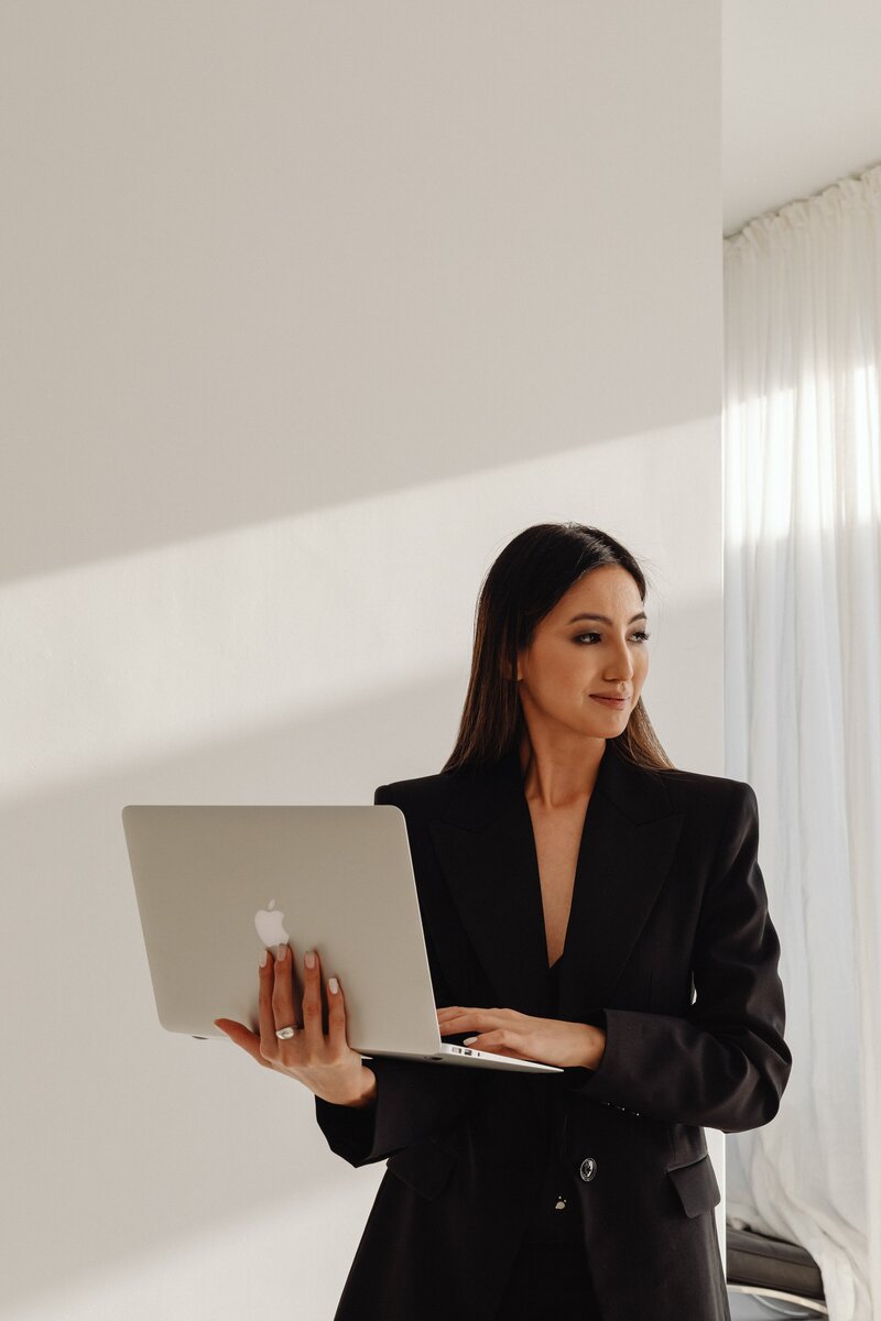 kaboompics_dark-classy-aesthetic-fashion-beautiful-asian-female-entrepreneur-in-black-suit-technology-and-devices-iphone-laptop-airpods-30065-min