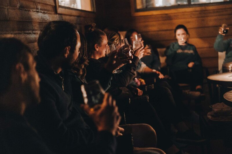 Dramatic and moody, a group of people sit around a fire talking to each other. 