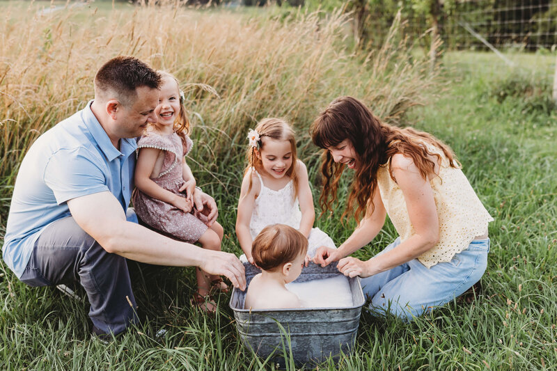 Mom holding her baby girl smiling in a beautiful glowing sun drenched sunflower field for her harrisburg family photo session