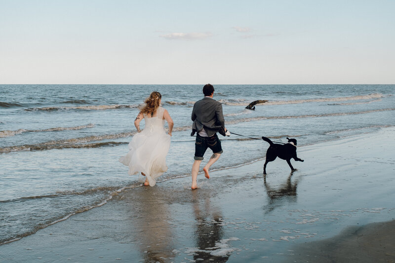 Wedding couple running on the beach with their dog
