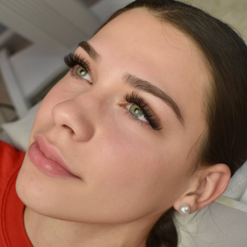 Client with dramatic lash extensions and soft glam finish, wearing pearl earring.